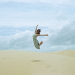 Joy Release - woman in white dress jumping on brown sand during daytime
