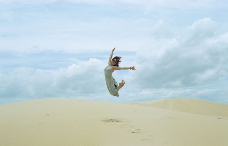 Joy Release - woman in white dress jumping on brown sand during daytime