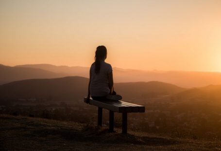 Travel Muse - woman sitting on bench over viewing mountain