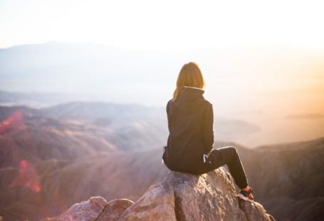 Emotional Balance - person sitting on top of gray rock overlooking mountain during daytime