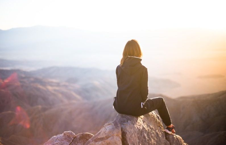 Emotional Balance - person sitting on top of gray rock overlooking mountain during daytime